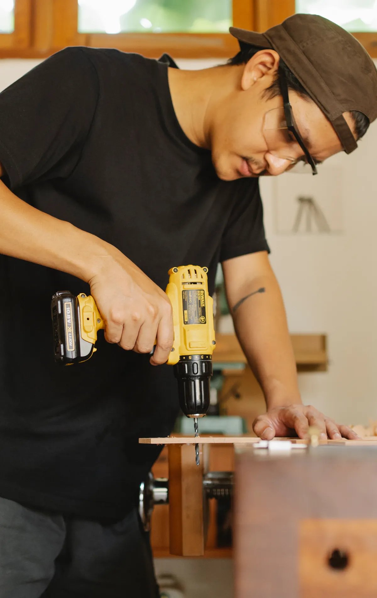 A craftsman in safety glasses carefully drilling a piece of wood