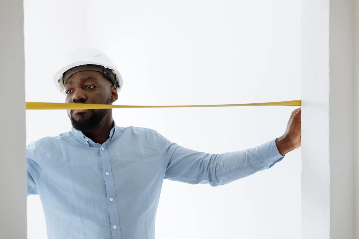A contractor measuring a wall with a tape measure during a walkthrough