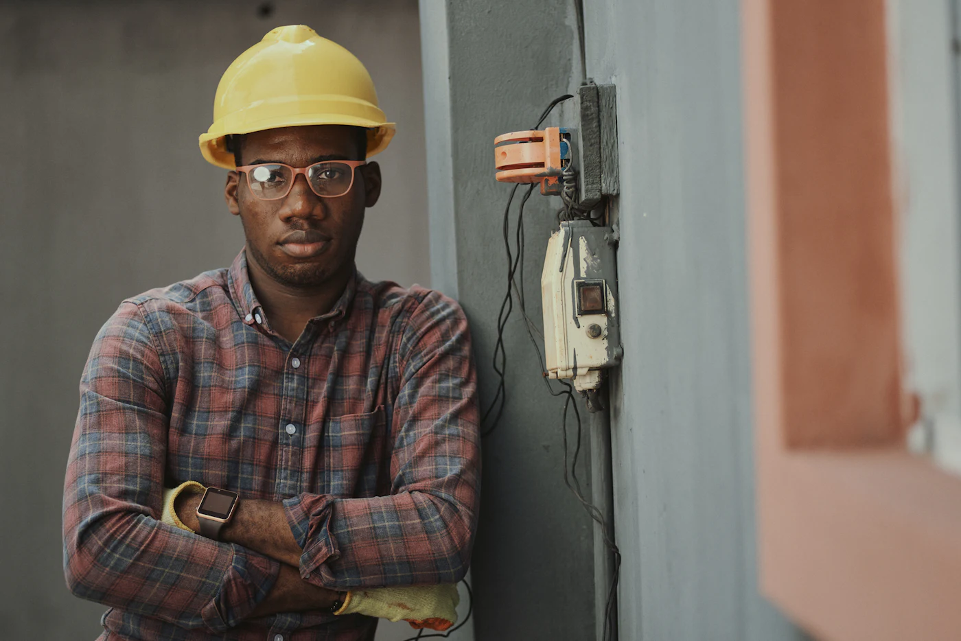 An electrician in a hard hat standing next to an electrical meter