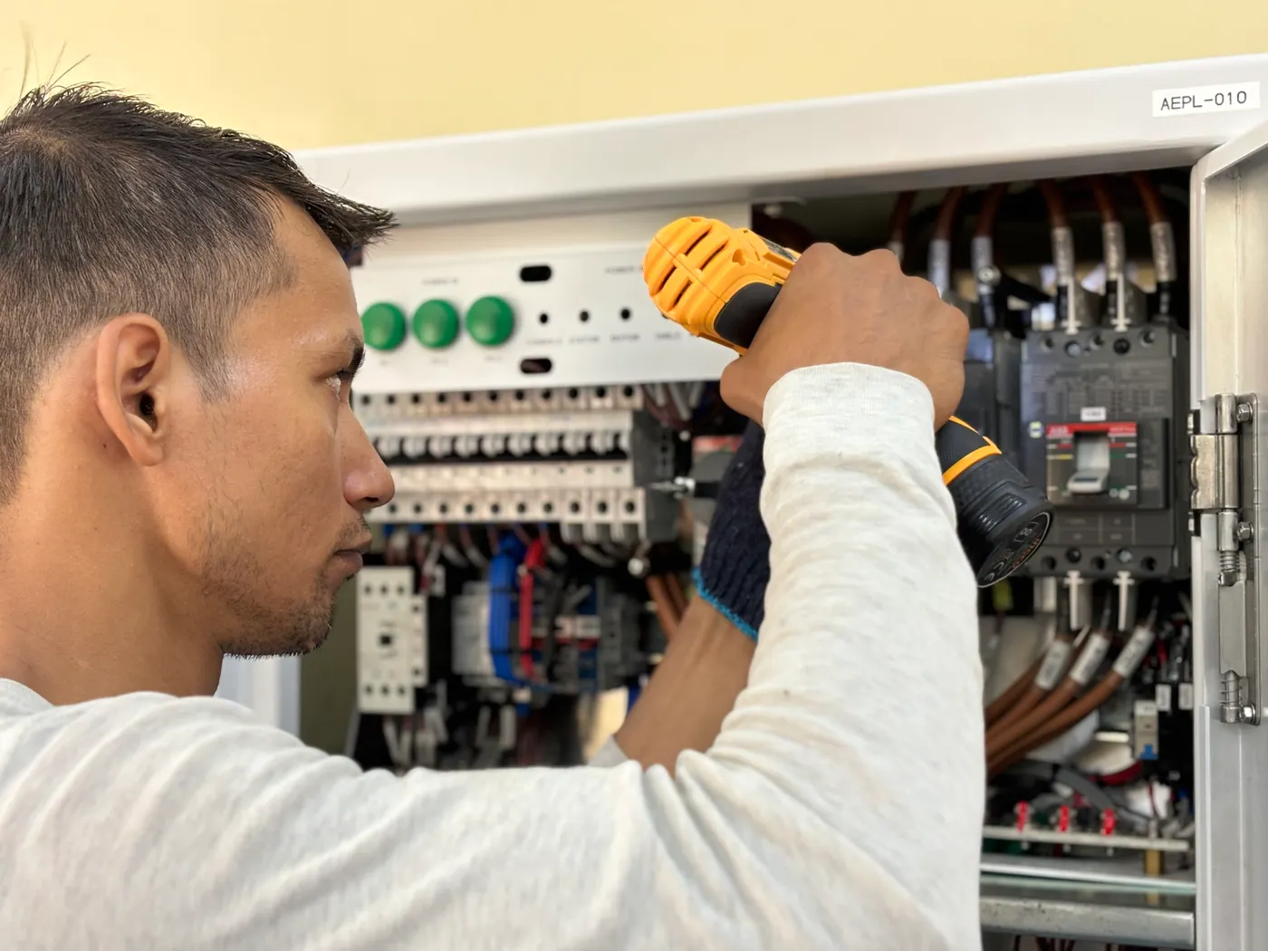 An electrician using a drill inside an electrical panel