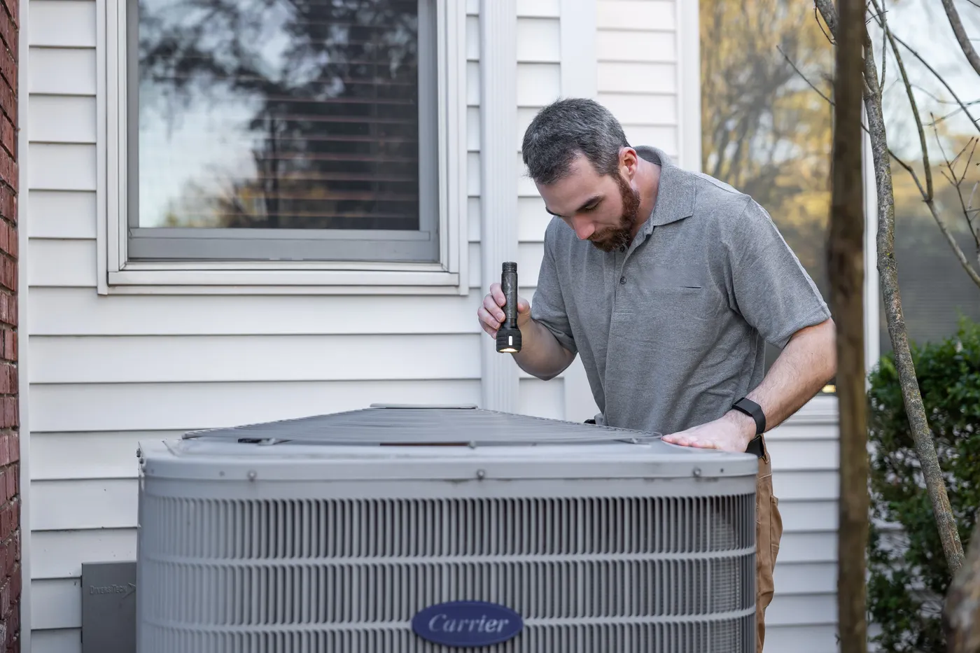 A technician inspecting an outdoor AC condenser beside a house
