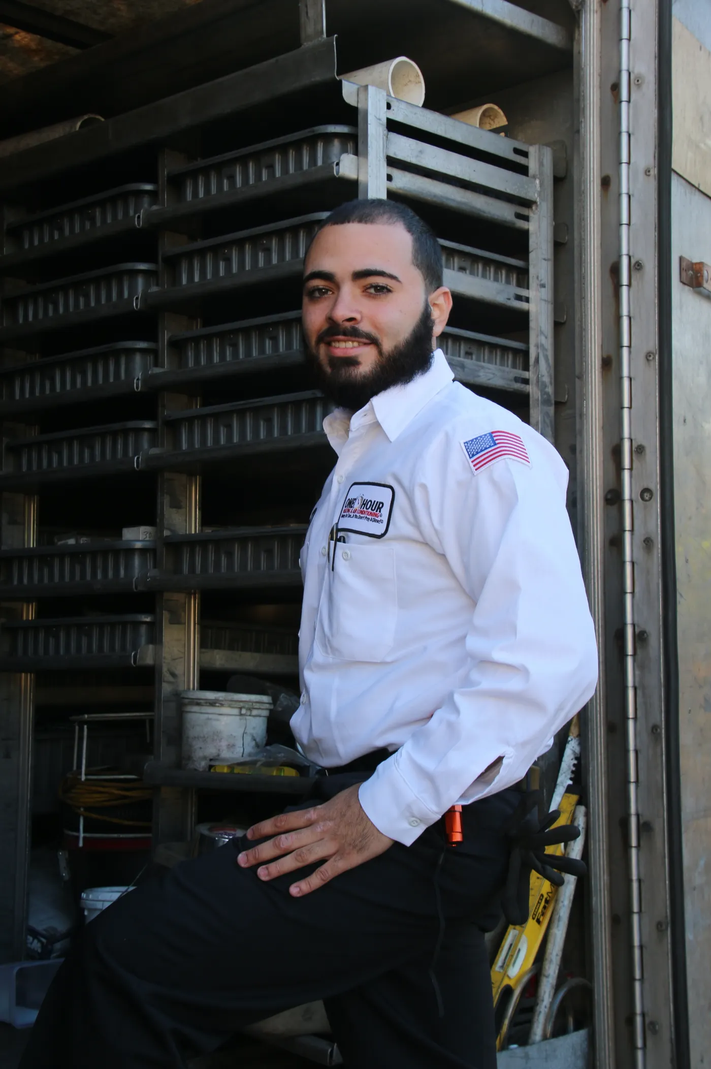 A smiling HVAC service technician standing at the back of his work truck