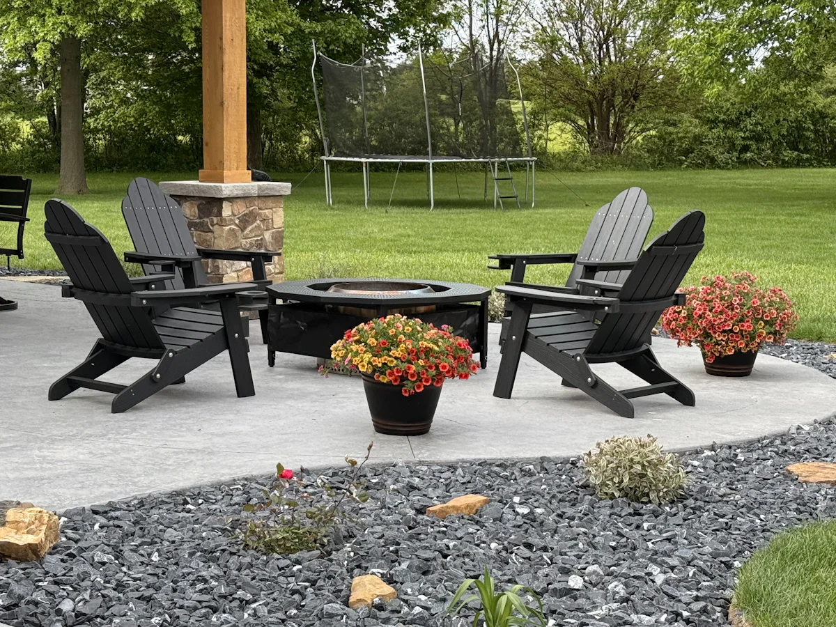 A finished backyard patio with a fire pit, Adirondack chairs, and flowers