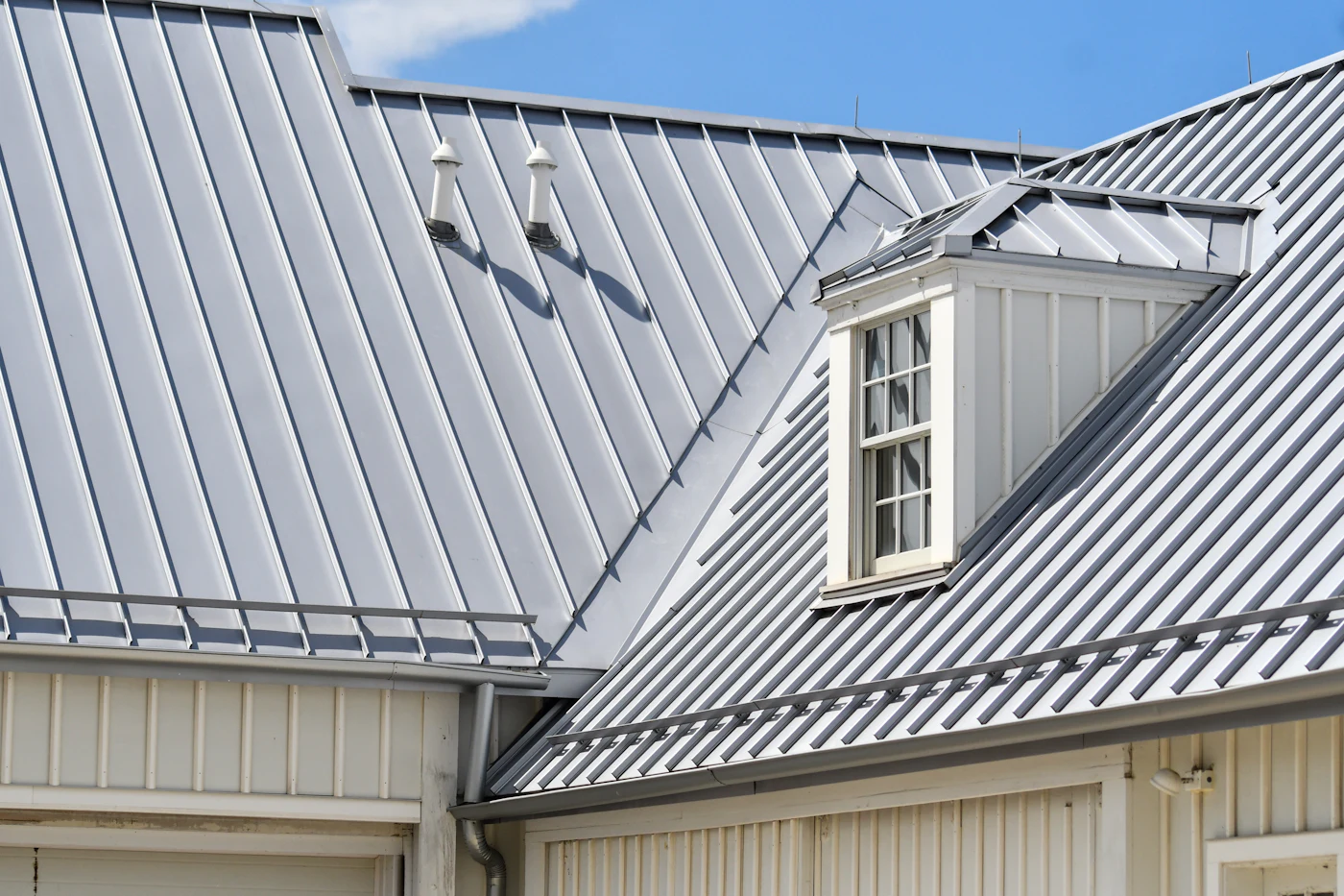 A gray metal roof with a dormer window on a white house